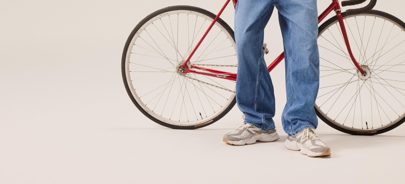Student in blue jeans standing in front of a red bicycle. 