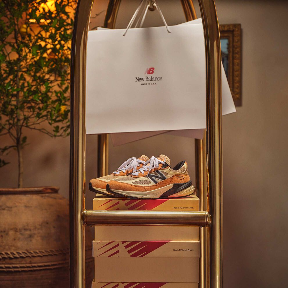Calzado y cajas de New Balance MADE in USA colocadas o colgadas en un carro de equipaje dorado en un agradable ambiente interior. 