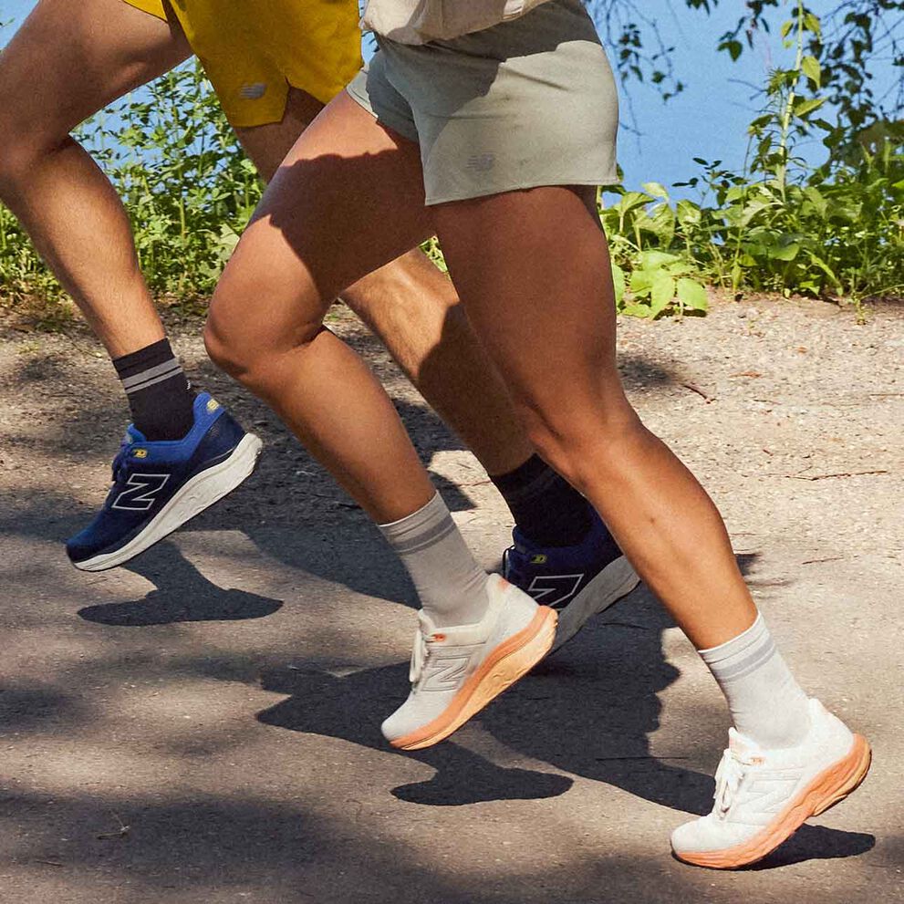 Two people wearing New Balance footwear and apparel running in a park. 