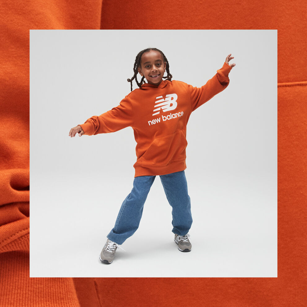 A young boy dancing in an orange and white NB Essentials Stacked Logo Hoodie and blue jeans. 