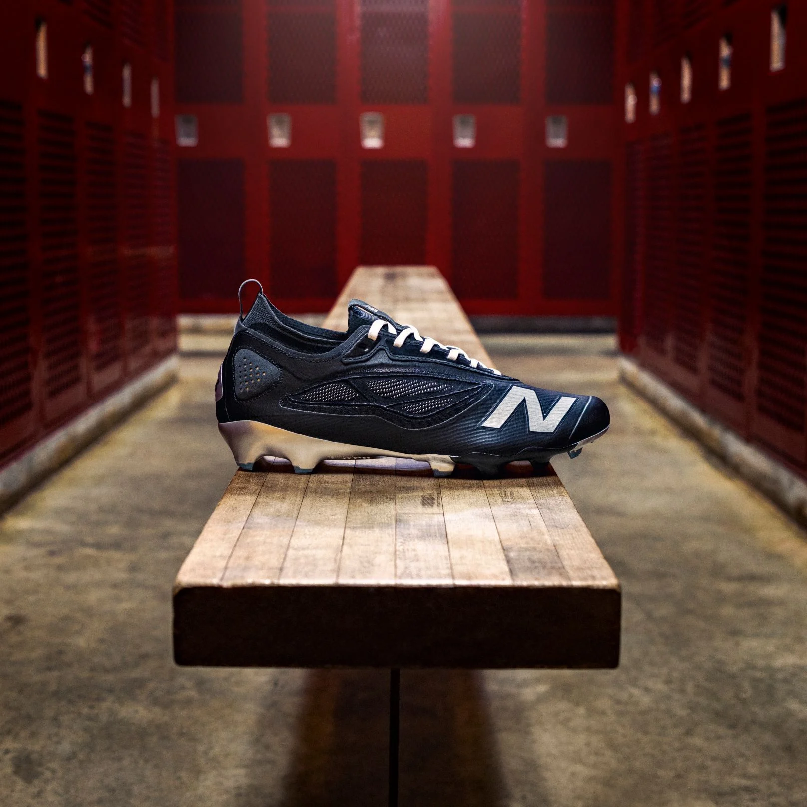 A black Rev X football cleat on a bench in a locker room.