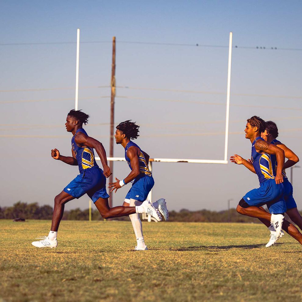 Atletas de fútbol americano de secundaria corriendo en un campo con tacos blancos de fútbol americano New Balance.