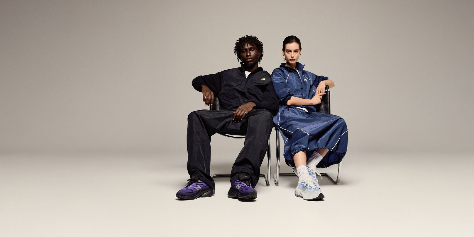 A man and a woman sitting in chairs on a beige background.