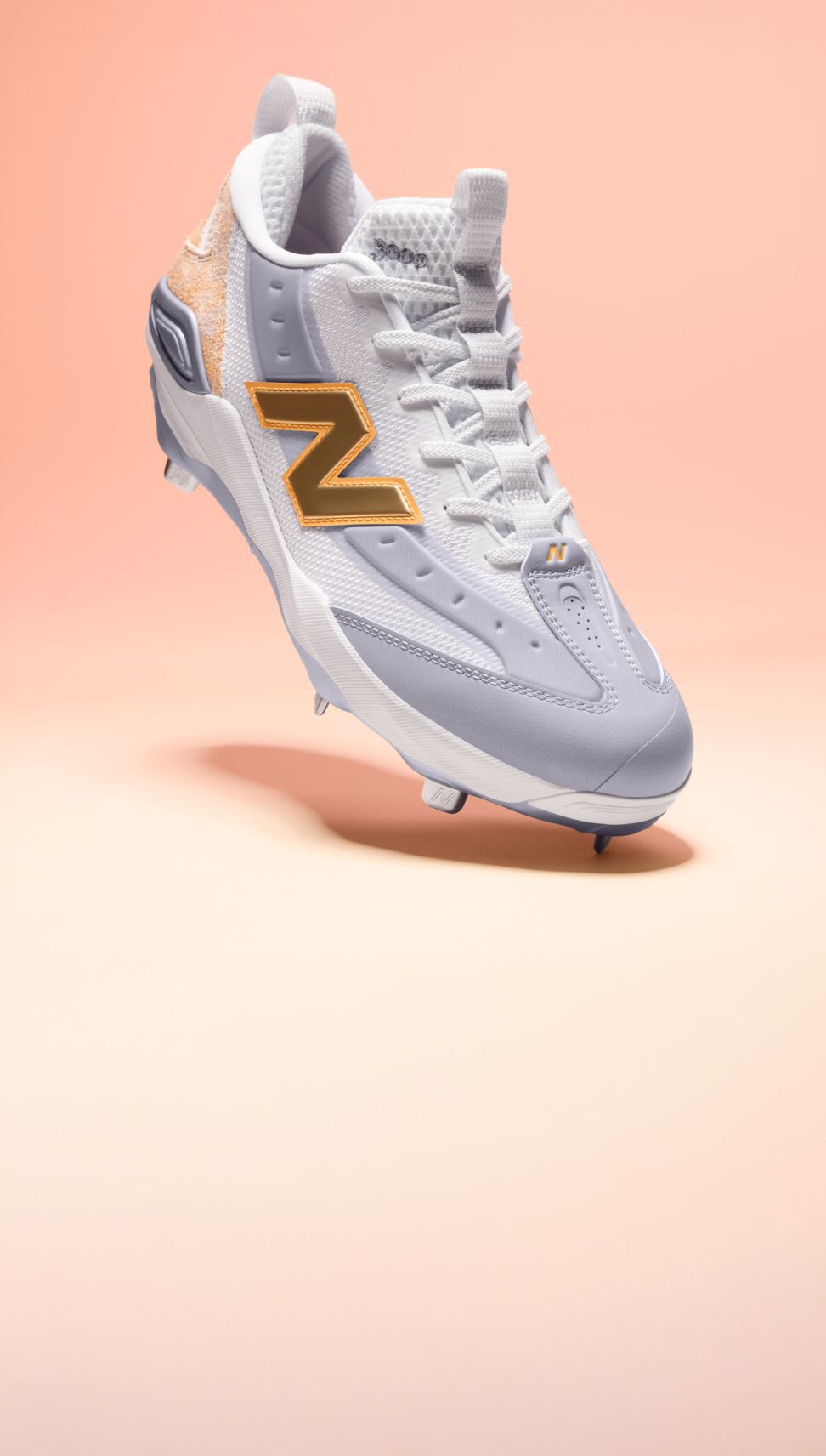 Side view of a single baseball cleat on a light pink gradient background.