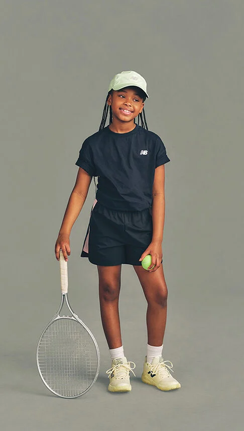 Kid holding a tennis racket against a grey studio background.