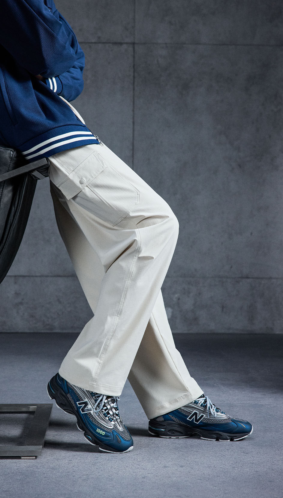 An individual, leaning on a chair, wearing New Balance 1000 sneakers