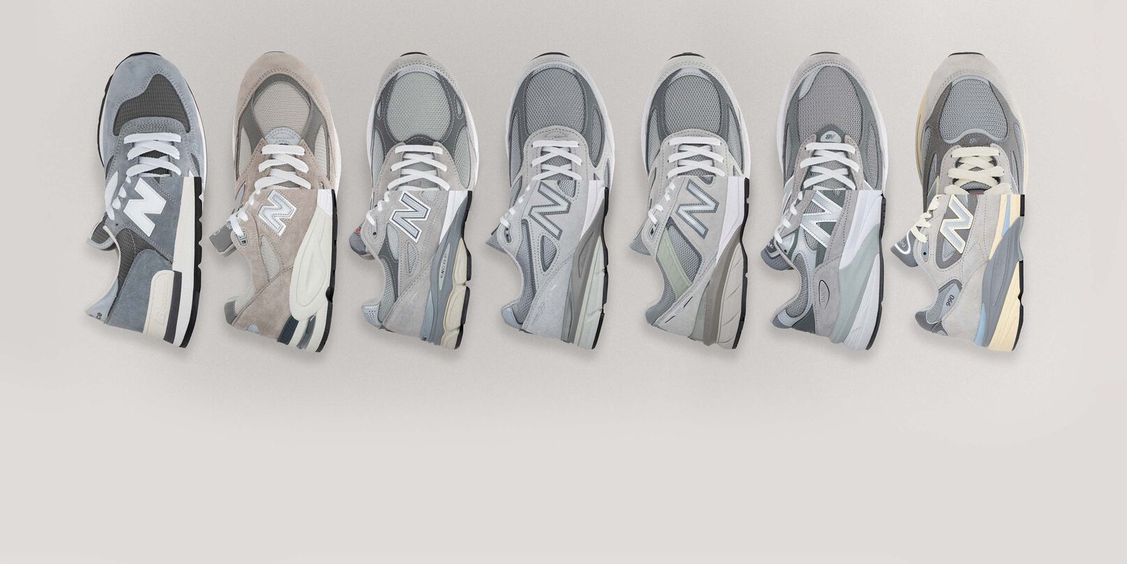 All seven generations of the 990 sneaker laying in a line on a grey backdrop.