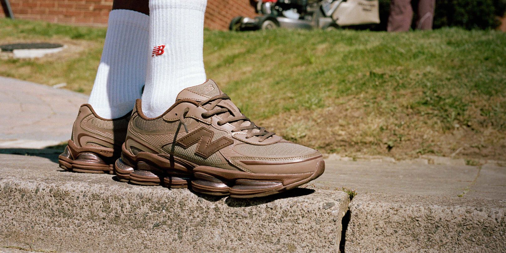 Imagen de rodilla hacia abajo de alguien que lleva unas zapatillas New Balance marrones al aire libre.