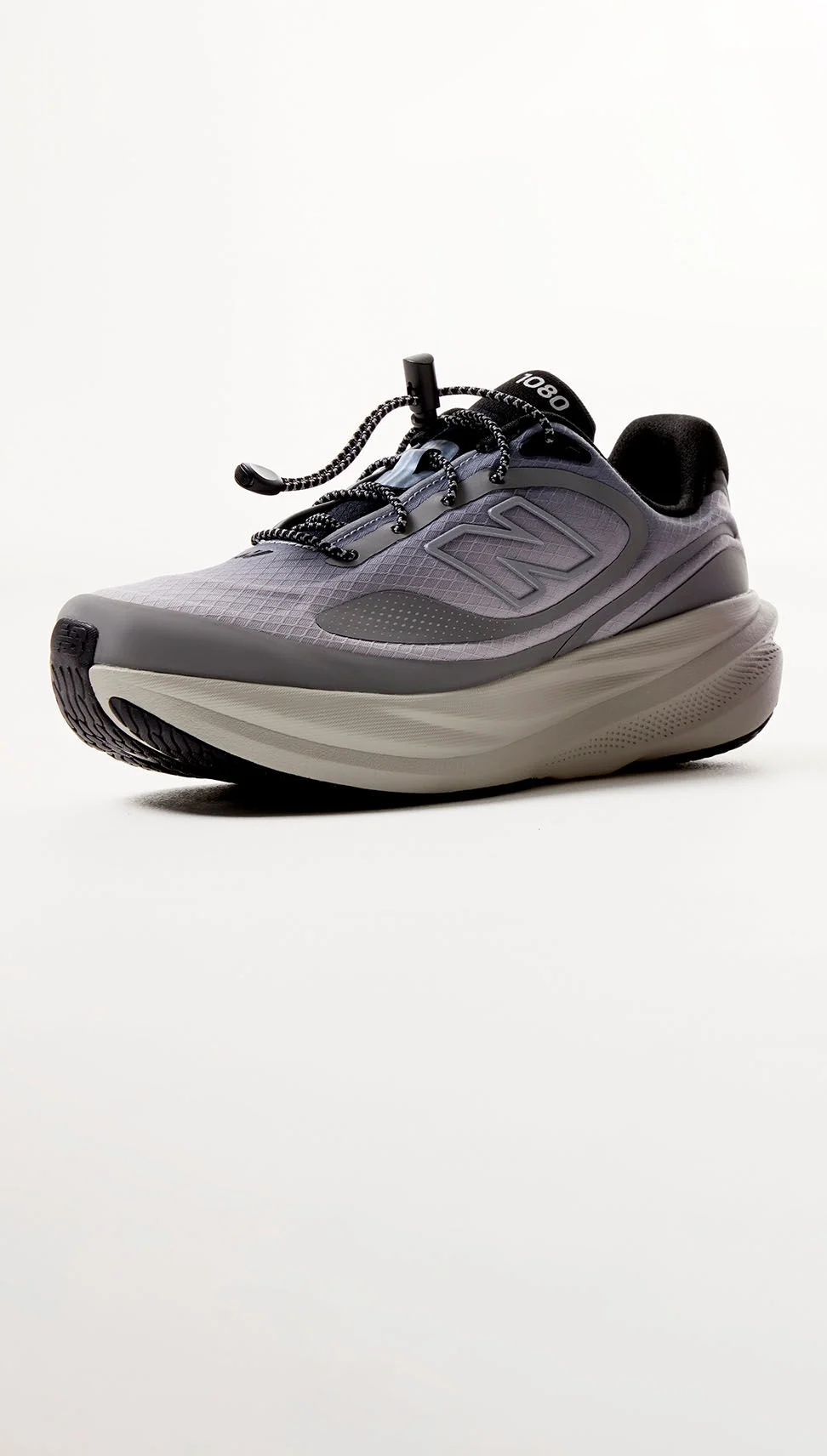 A grey colored shoe sitting against a grey studio backdrop. 