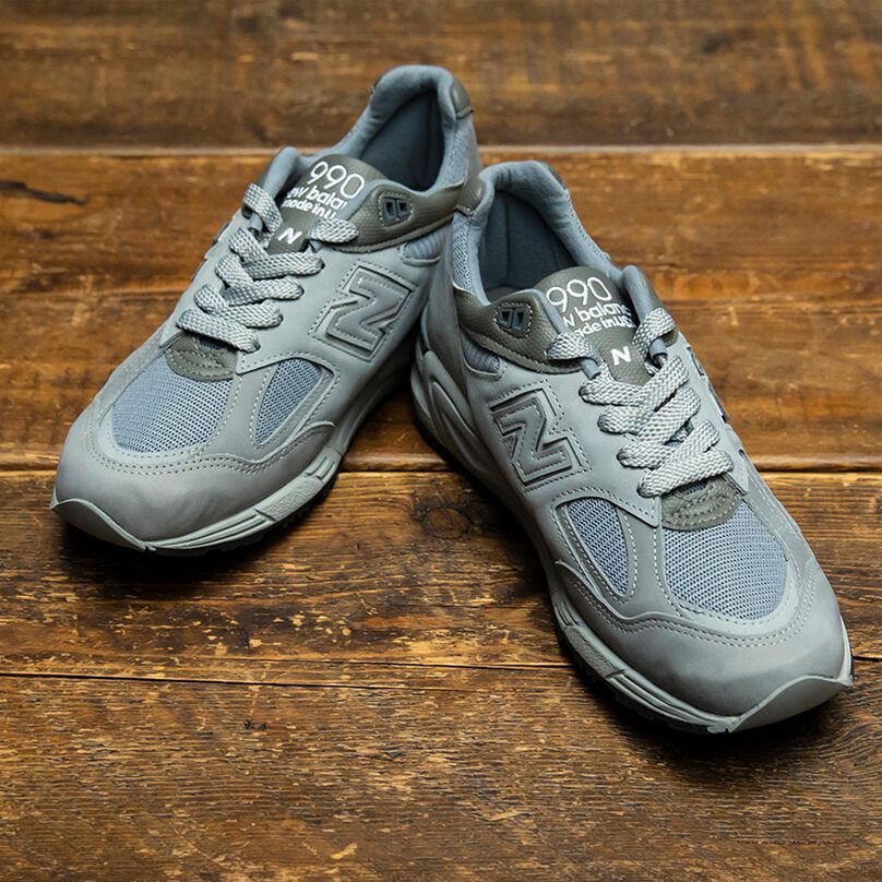 Overhead view of a pair of grey NB x WTAPS 990v2 sneakers sitting on rustic wood flooring