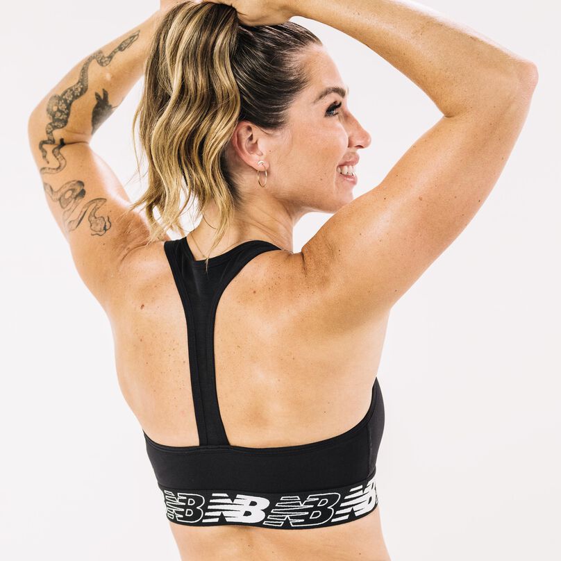 Woman turned from camera with arms raised up showing the back closure/fit of a black NB Pace bra.