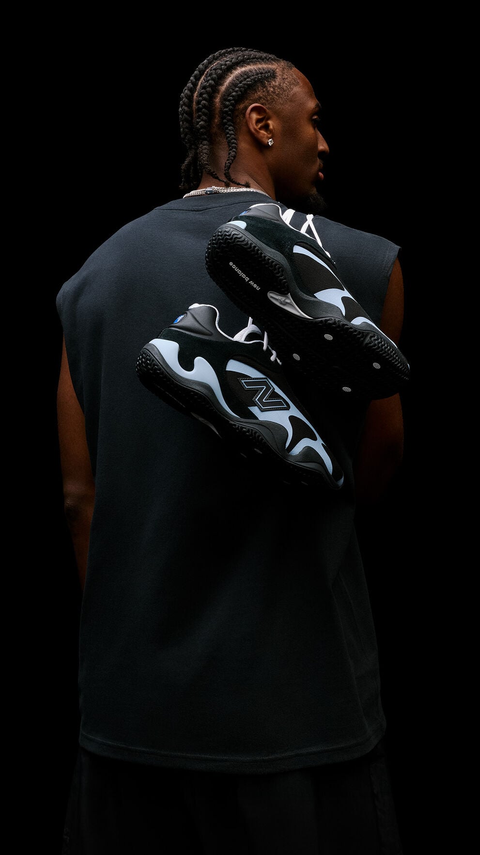 Studio portrait from behind featuring black-and-light-blue athletic sneakers suspended across a person's back against a black background.