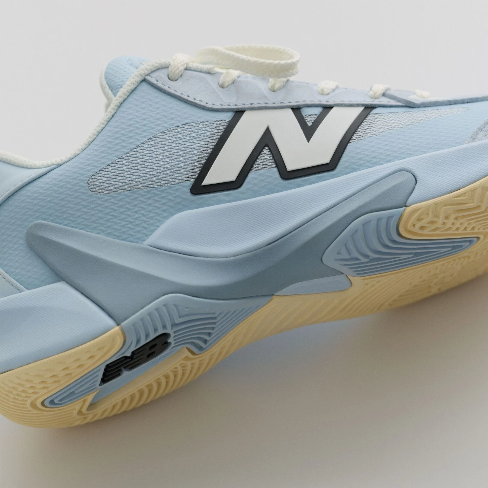 Close-up side view of a light blue New Balance basketball shoe featuring a mesh upper, large logo, and gum rubber outsole.