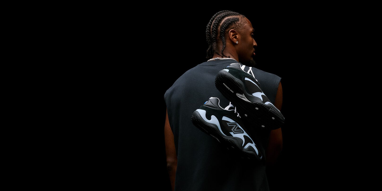 Studio portrait from behind featuring black-and-light-blue athletic sneakers suspended across a person's back against a black background.