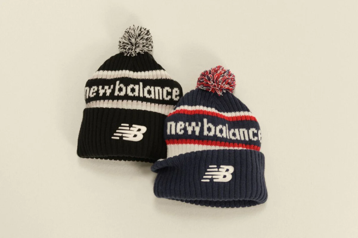Two New Balance knit pom beanies in black-and-white and navy-red-and-white displayed against a clean neutral background.