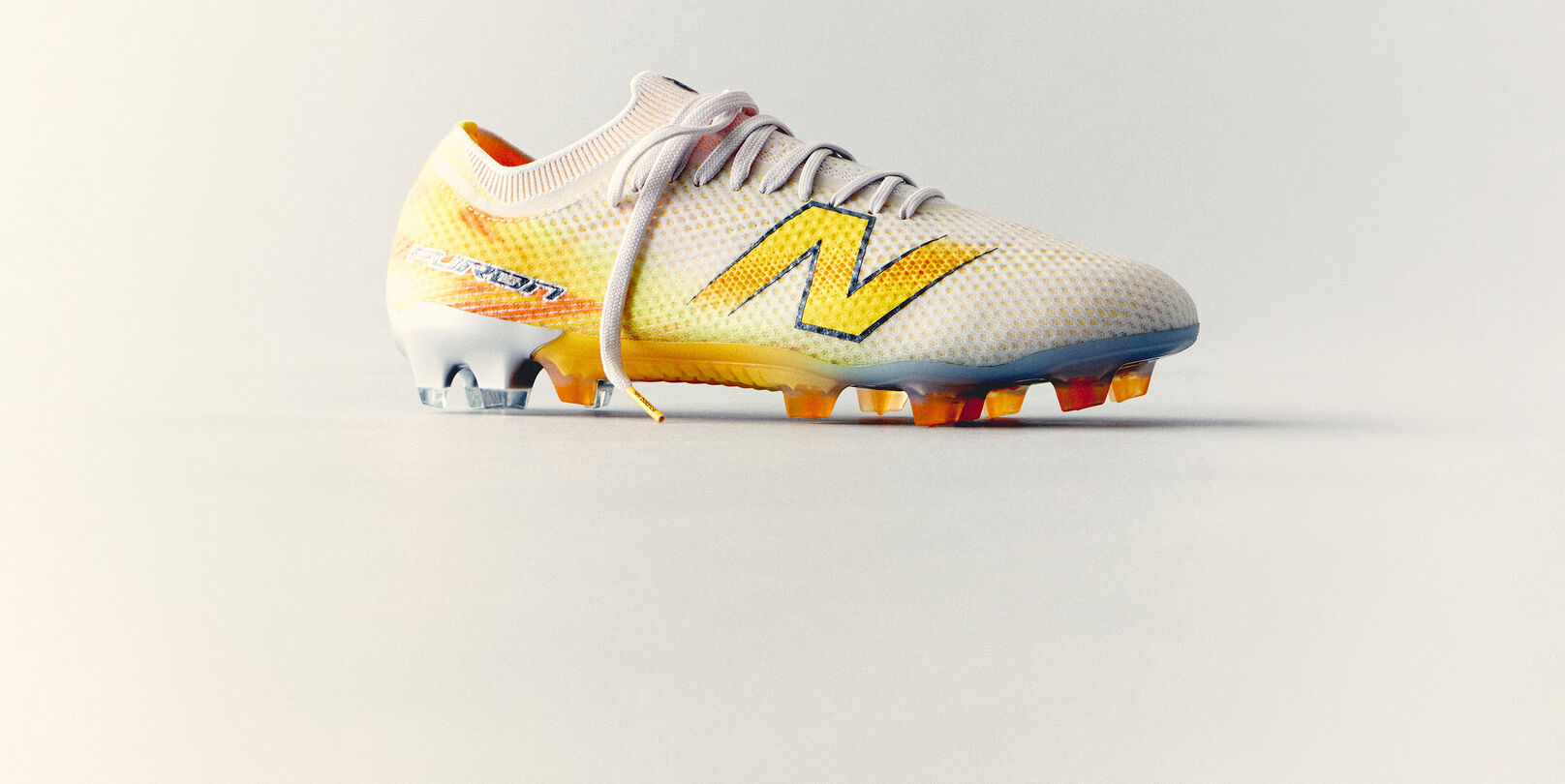 White and yellow New Balance soccer cleat with a lightweight mesh upper and molded studs displayed against a clean white background.