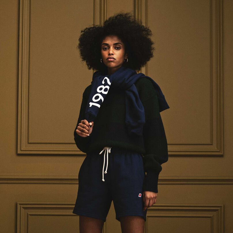 A woman standing in a beautiful indoor environment with a navy MADE in USA heritage shirt drapped around her neck.