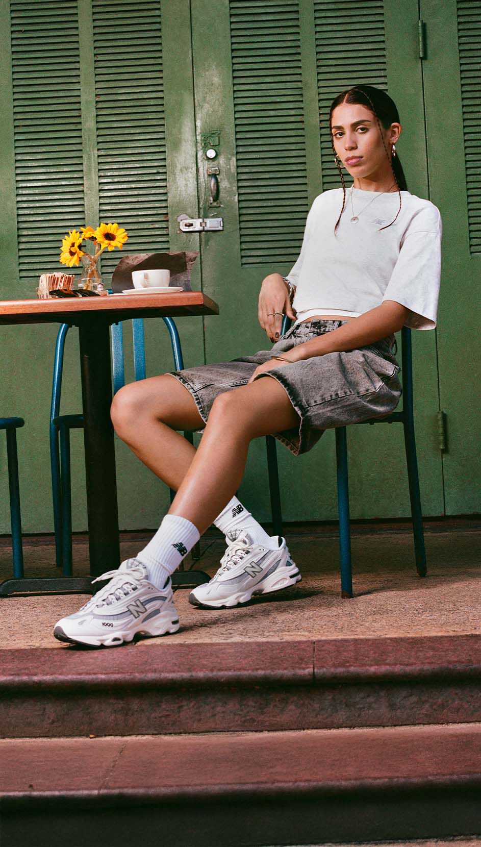 Una persona sentada en una mesa de café, con un par de zapatillas New Balance 1000. 