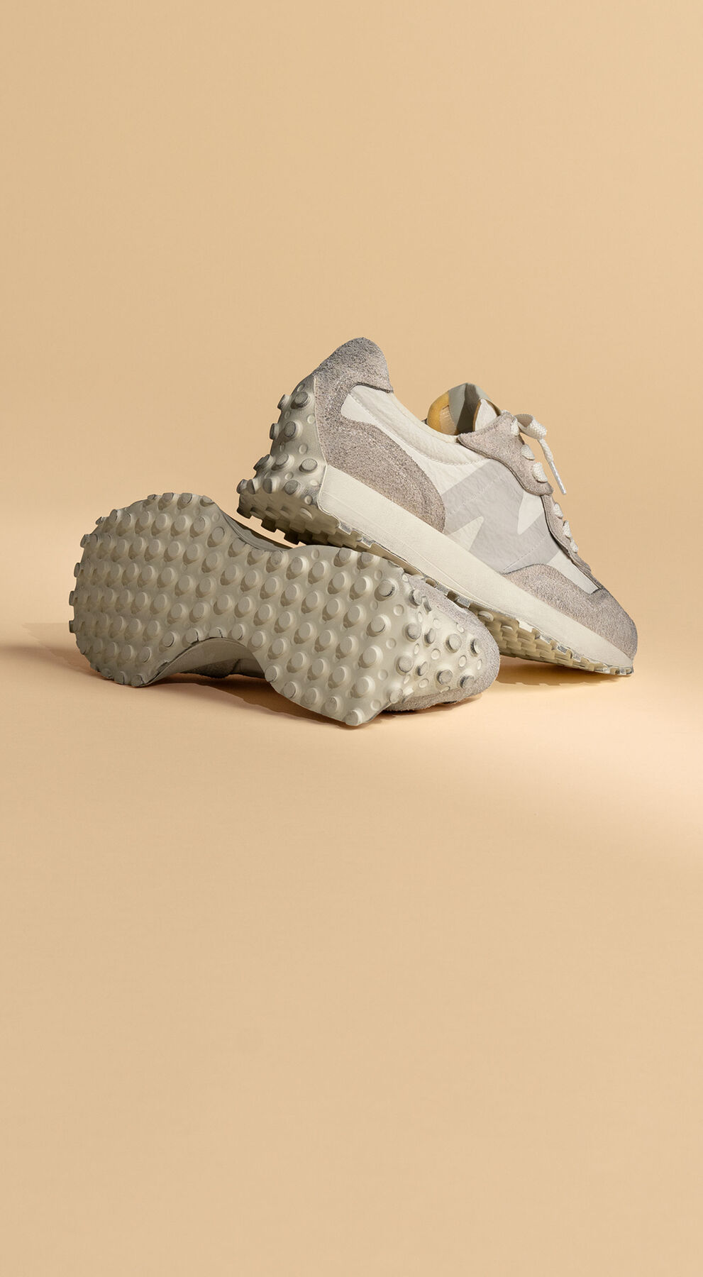Pair of grey New Balance 327 shoes propped up against a beige studio background