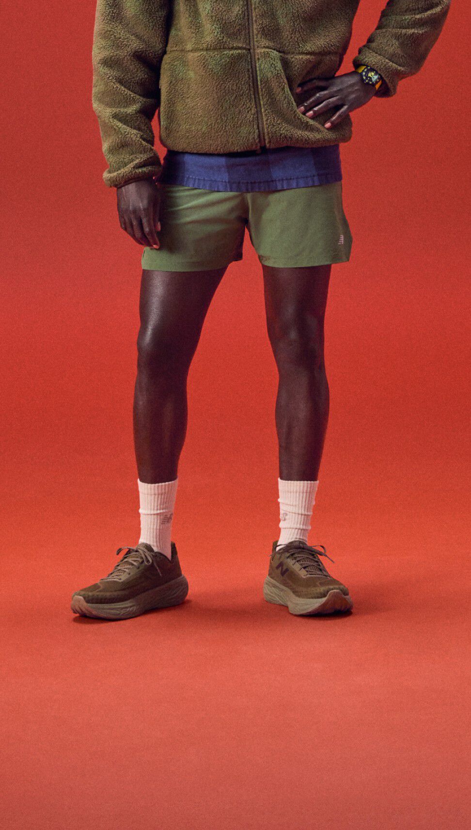 Joven de pie sobre un fondo rojo con una sudadera con capucha verde.