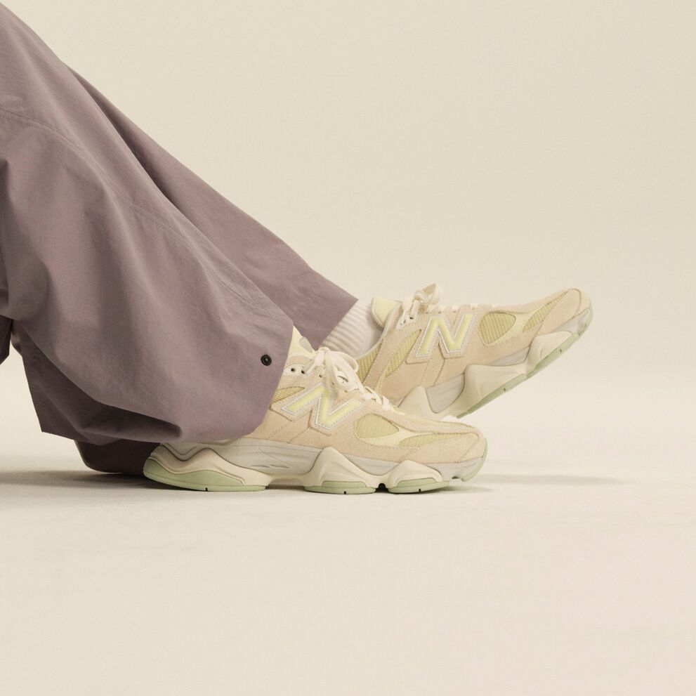 Close-up of cream New Balance athletic sneakers paired with white crew socks and lavender wide-leg pants in a clean studio setting.