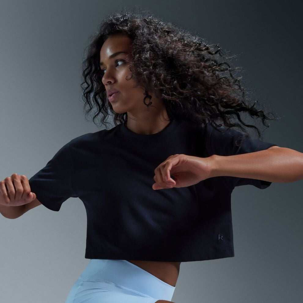 Woman in motion wearing a cropped black athletic t‑shirt and light athletic shorts.