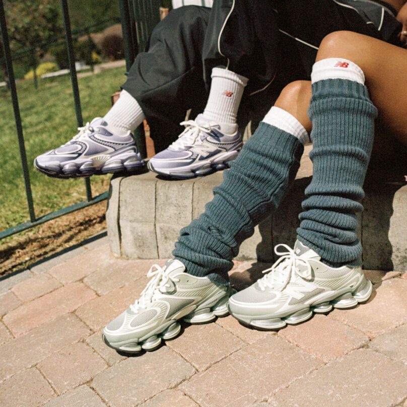 Two people sitting on a sidewalk wearing New Balance sneakers.