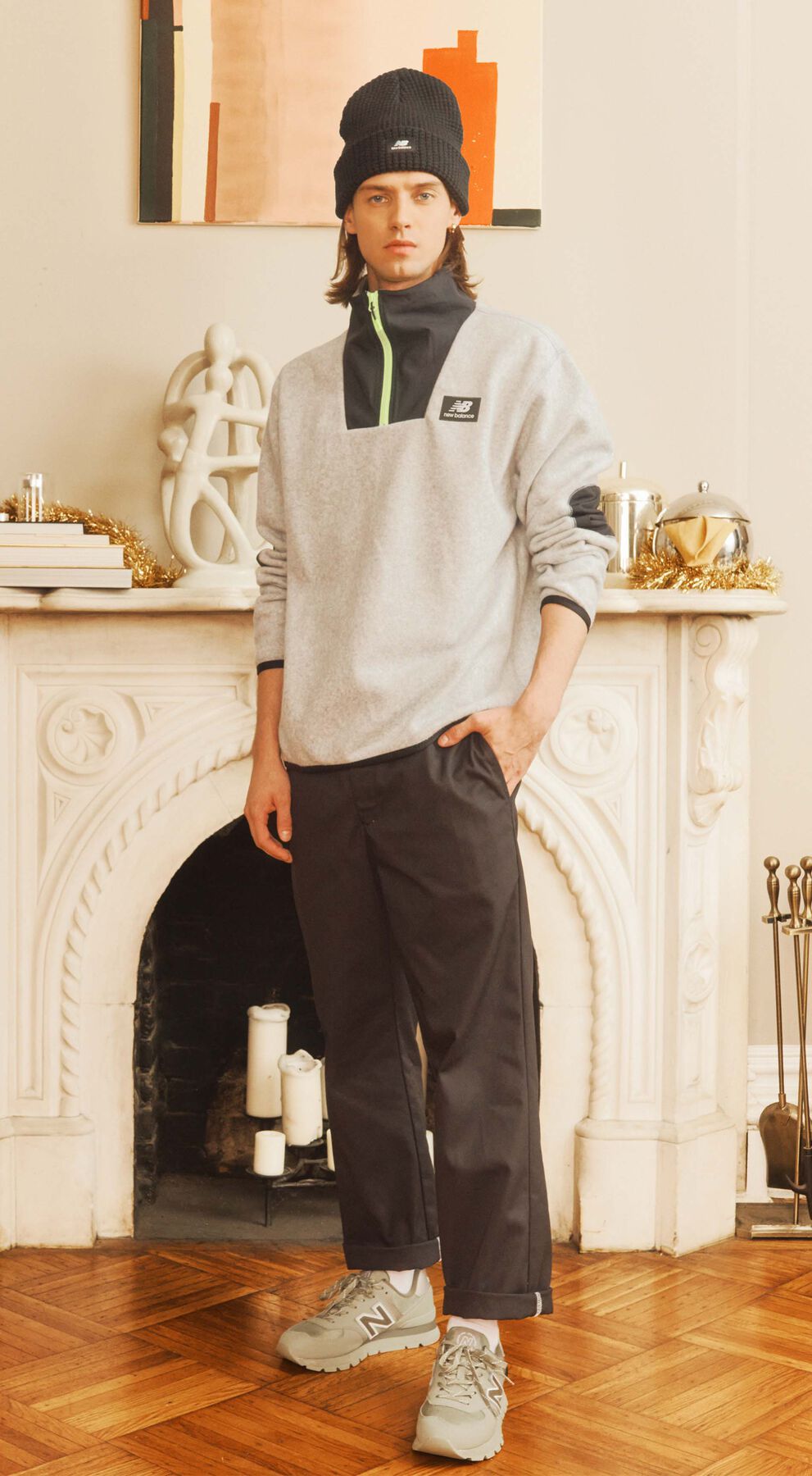 Male model wearing cold weather New Balance outdoor clothing and shoes posed against a decorative fireplace