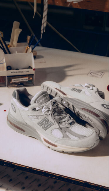 A pair of New Balance Made in UK sneakers on a white workbench surrounded by shoemaking tools and other textile equipment. 