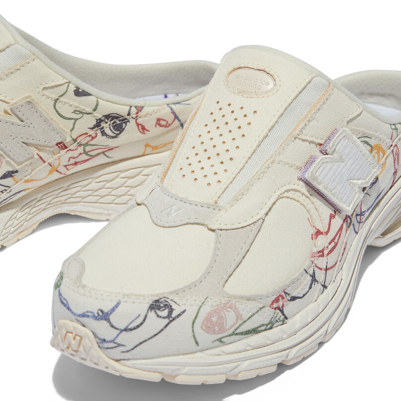 Cropped view of the upper a cream colored mule shoe with embroidered art on the shoe
