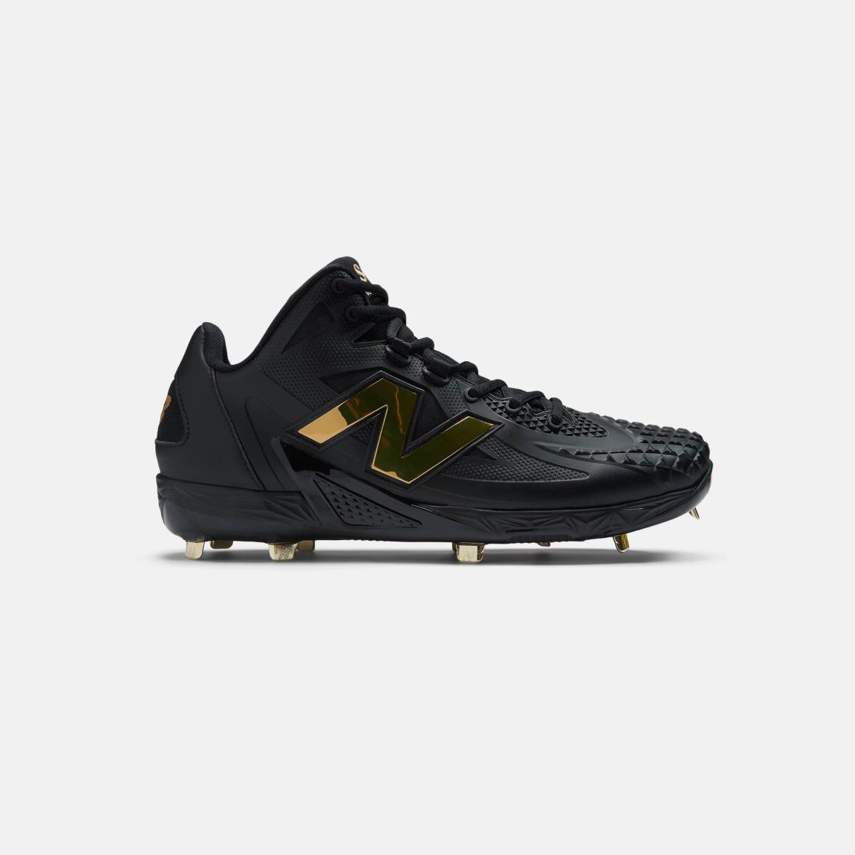 Black low-cut baseball cleat with gold New Balance logo accents and metal spikes on the outsole, shown in side profile against a white background.