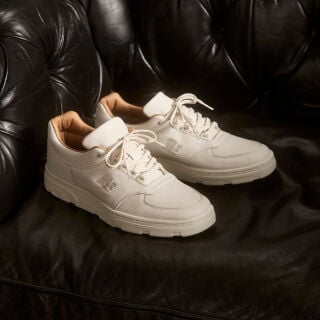 Knee down view of a woman wearing a pair of New Balance Made in UK sneakers standing in a beige studio environment.