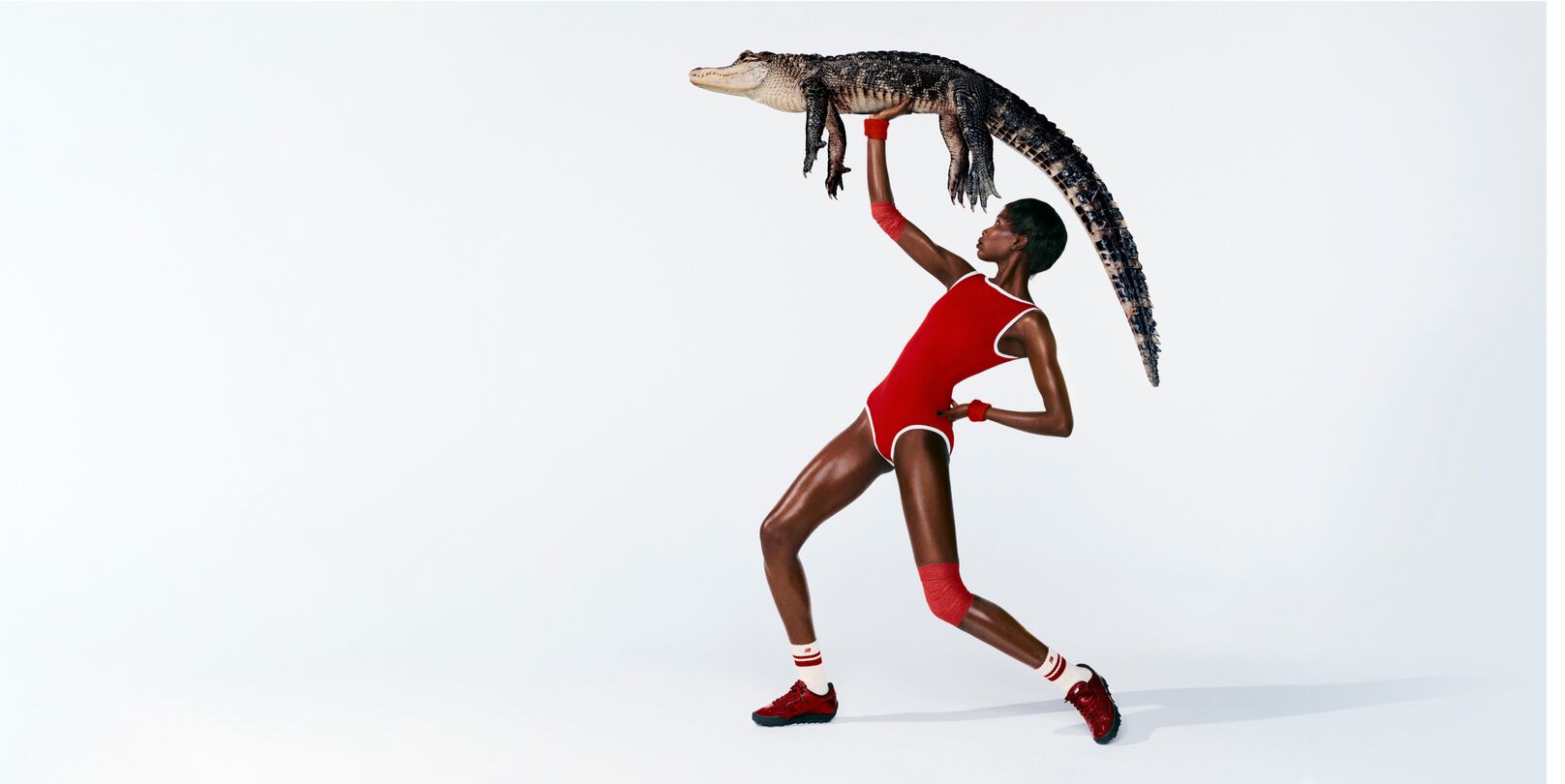 A woman in front of a white background wearing Gator Run shoes while holding an alligator.