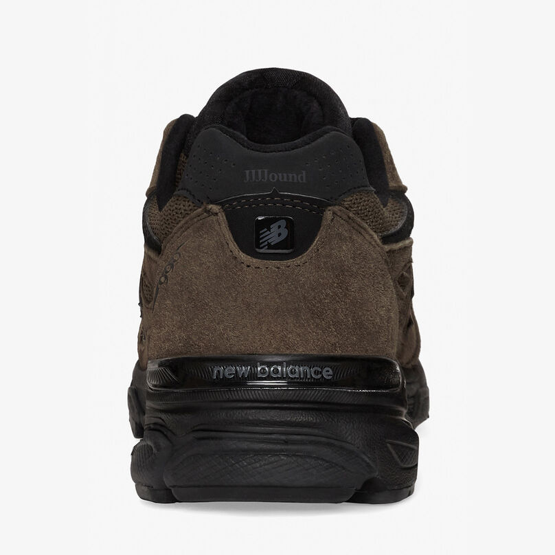 Single brown 990v3 shoe posed against a grey studio background shown from the back to highlight detail in heel
