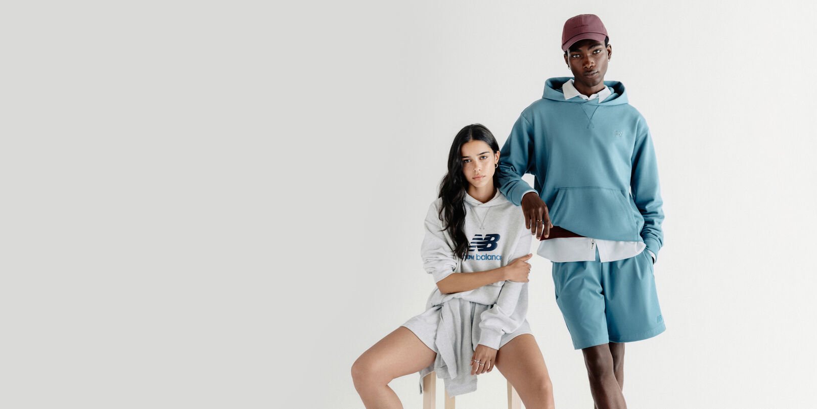 A man standing and a woman sitting on a stool in front of a grey studio backdrop.