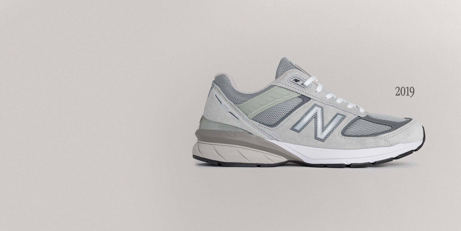 A grey 990v5 sneaker sitting on a grey background.