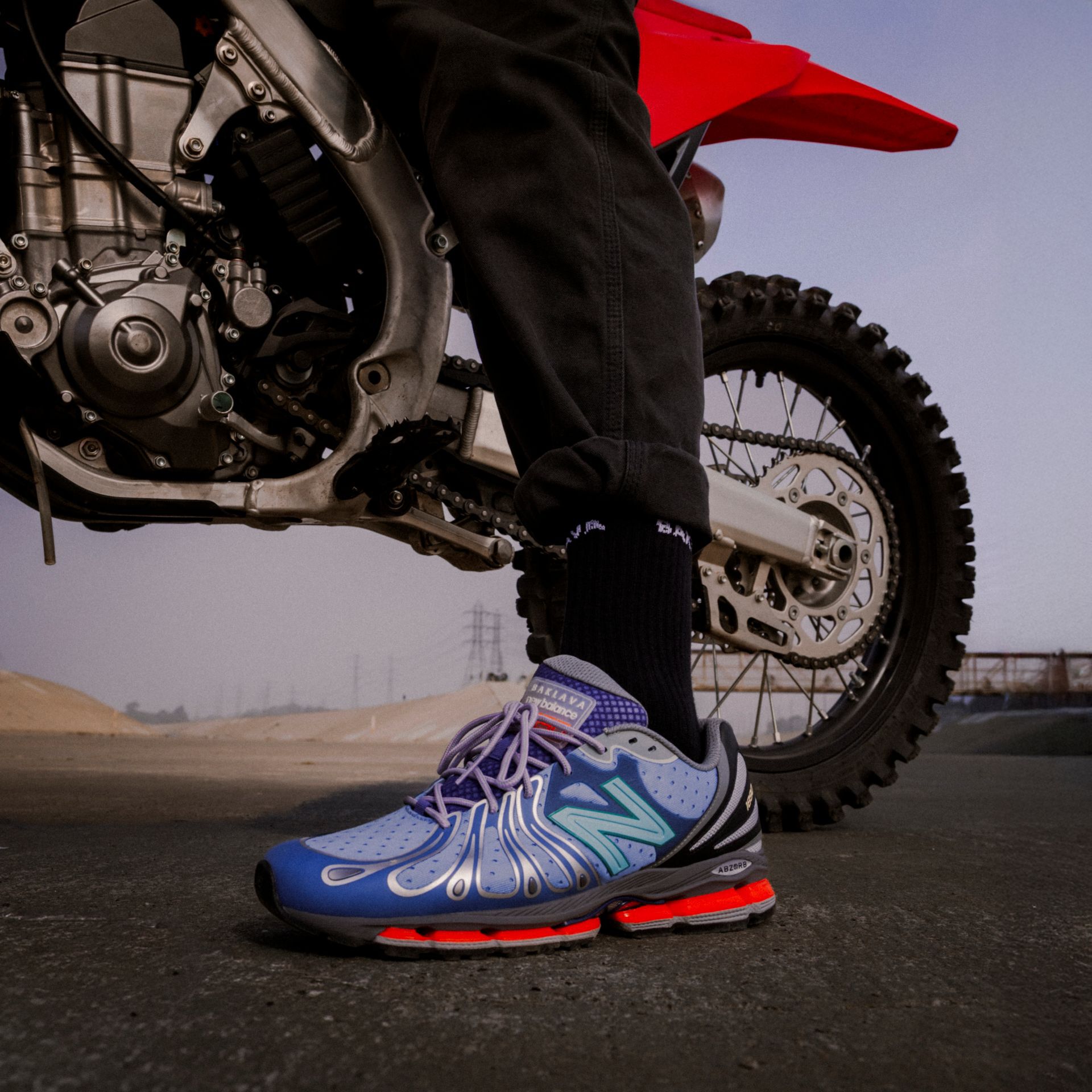 Knee down image of a person wearing a blue BAKLAVA x New Balance 1890 shoe.