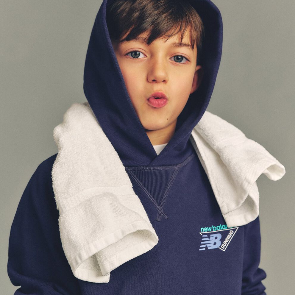 Imagen de estudio en primer plano de un ni&ntilde;o con una sudadera azul marino con capucha y el logo "New Balance Running" impreso en el pecho.