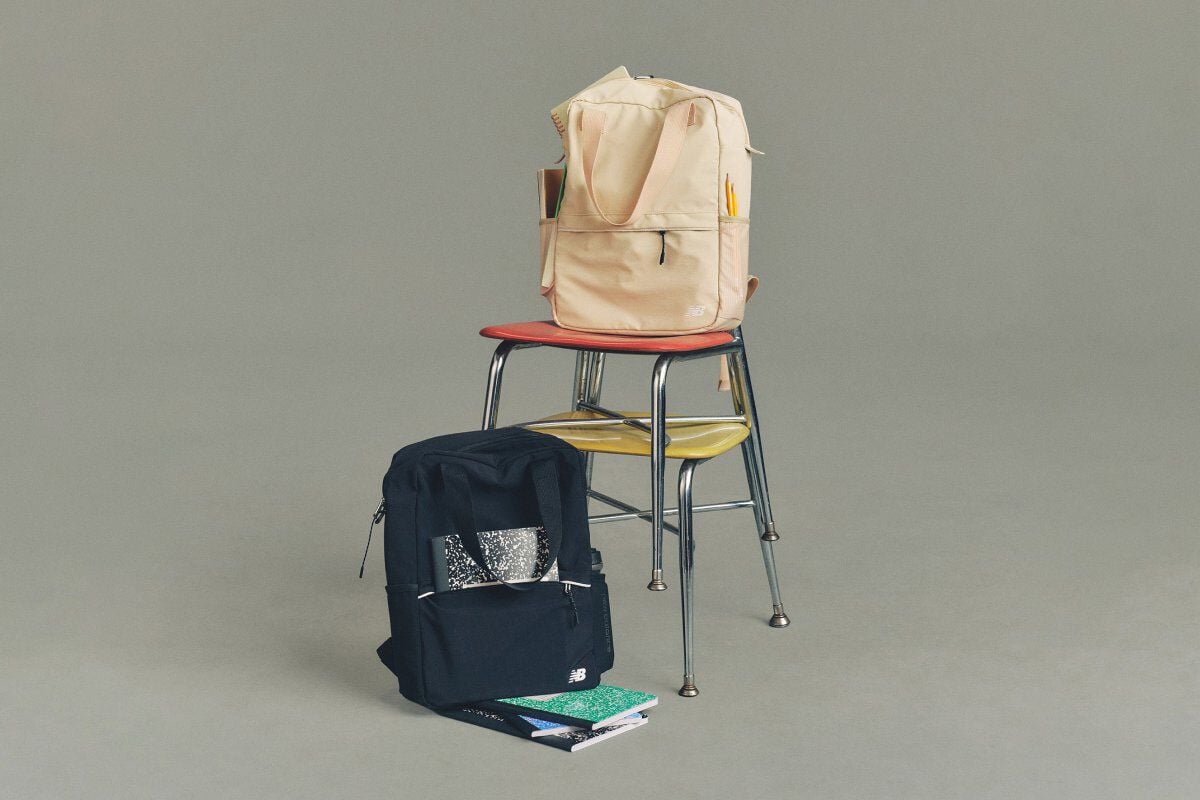 Studio image of a cream colored and a navy colored New Balance backpack placed on a metal chair.