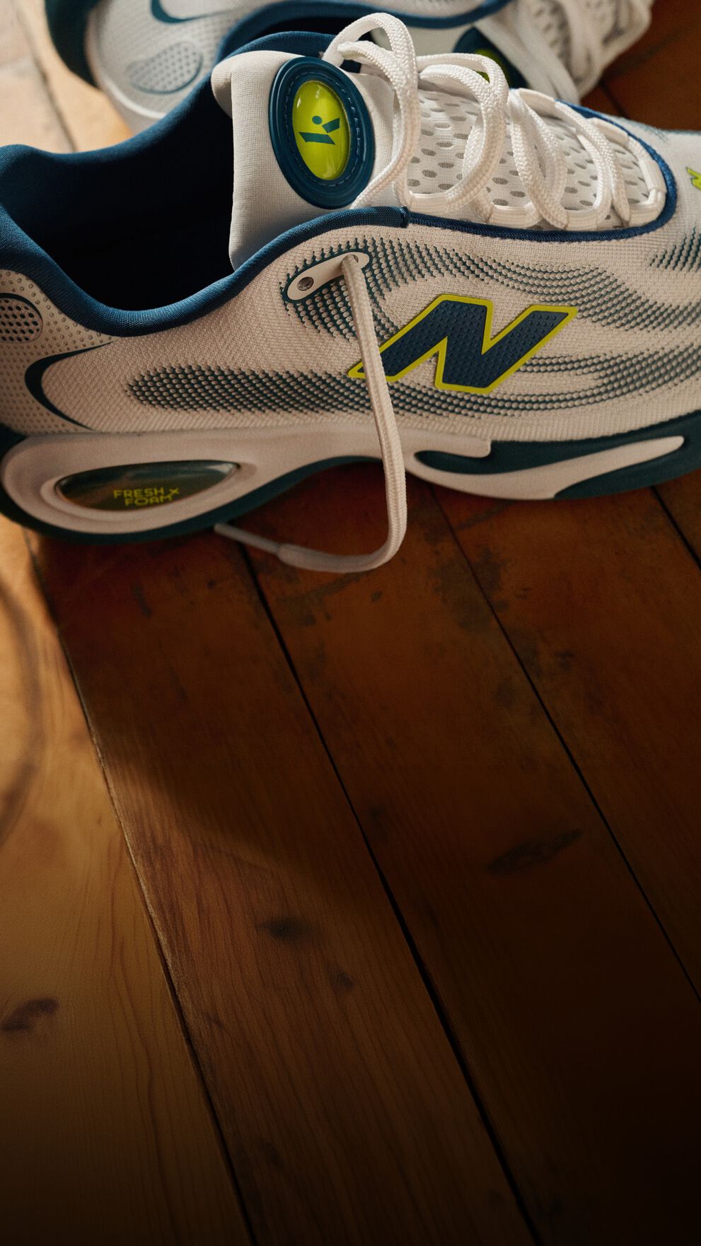 Close-up of New Balance training shoes placed beside a dumbbell and workout equipment on a hardwood gym floor.
