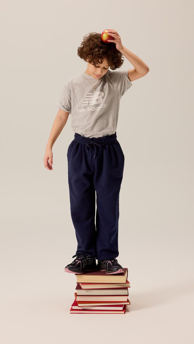 Kid standing on a pile of books while holding an apple on his head. 