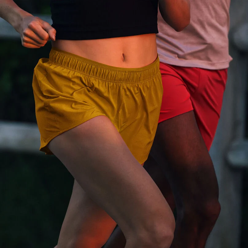 Two individuals running outside, wearing New Balance RC Shorts.