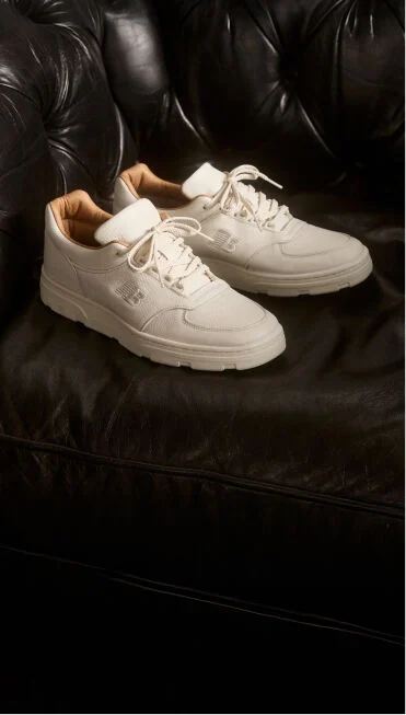 A pair of New Balance Made in UK sneakers sitting on a black leather sofa. 