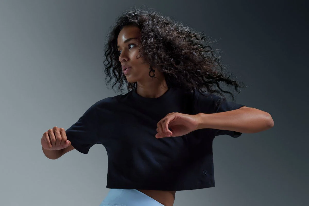 Woman in motion wearing a cropped black athletic t‑shirt and light athletic shorts.