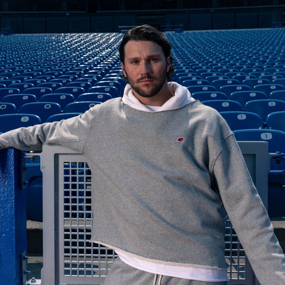 Young male athlete in a grey hoodie leaning on a stadium fence.