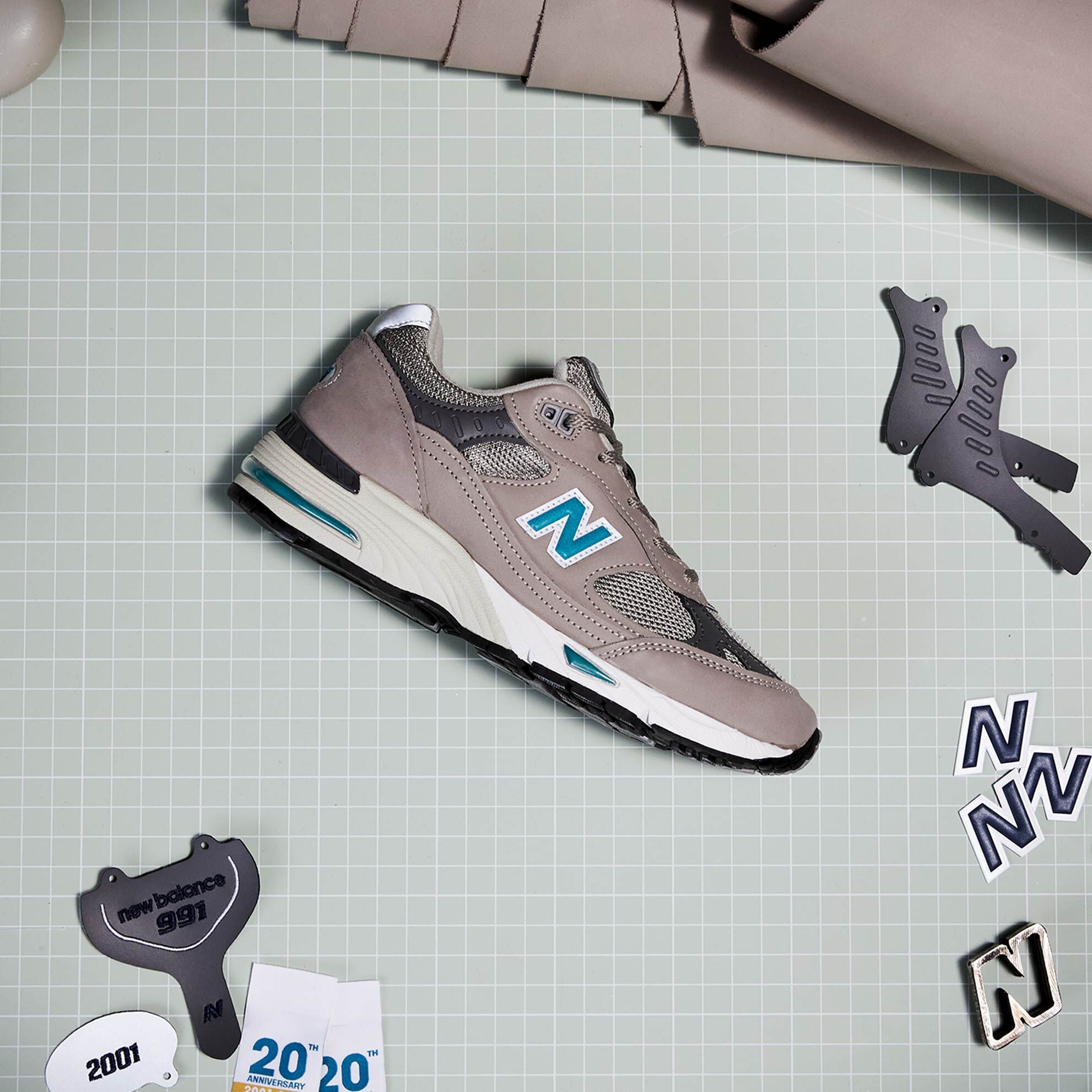 A women’s grey NB 991 sneaker sitting on a grid-lined cutting mat amongst the parts and pieces from which it was constructed