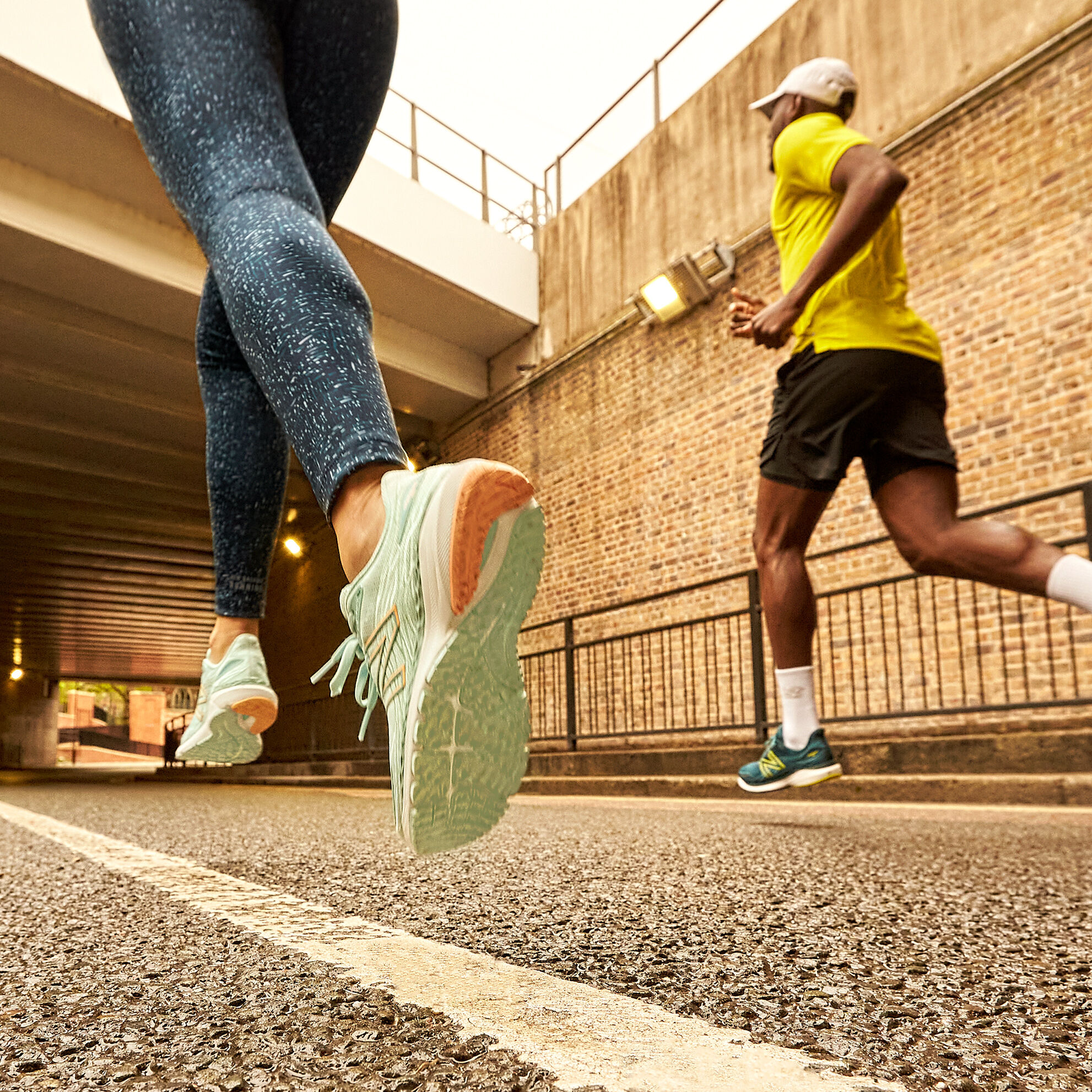 Knee down crop of a female and male runner, female wearing patterned blue leggings and light blue Fresh Foam X 860v12 and male wearing a yellow shirt, black shorts and dark green Fresh Foam X 860v12