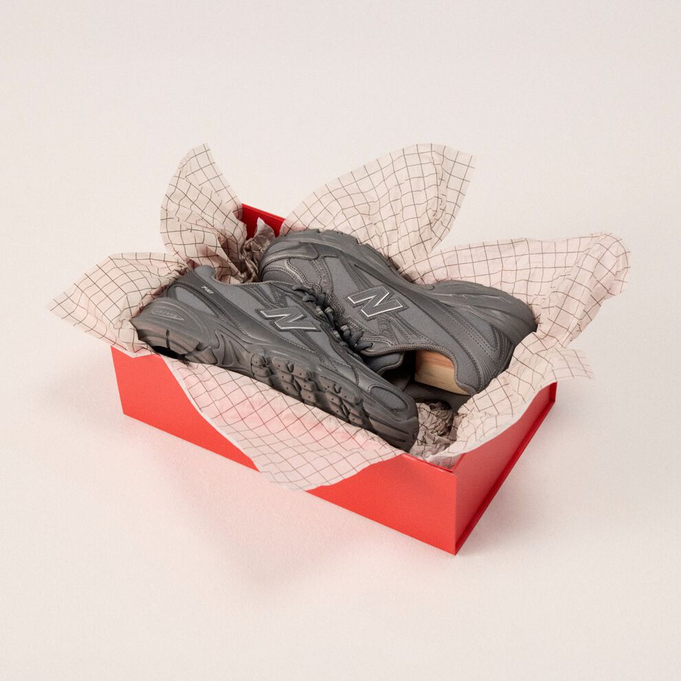 Par de zapatos grises en caja con papel de regalo.