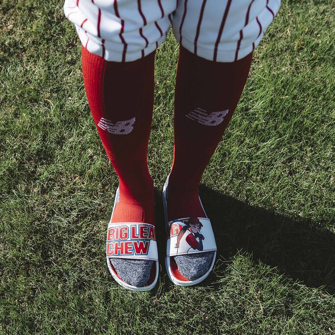 Top down shot of person’s legs wearing the Big League Chew slides in knee high red socks and baseball uniform.