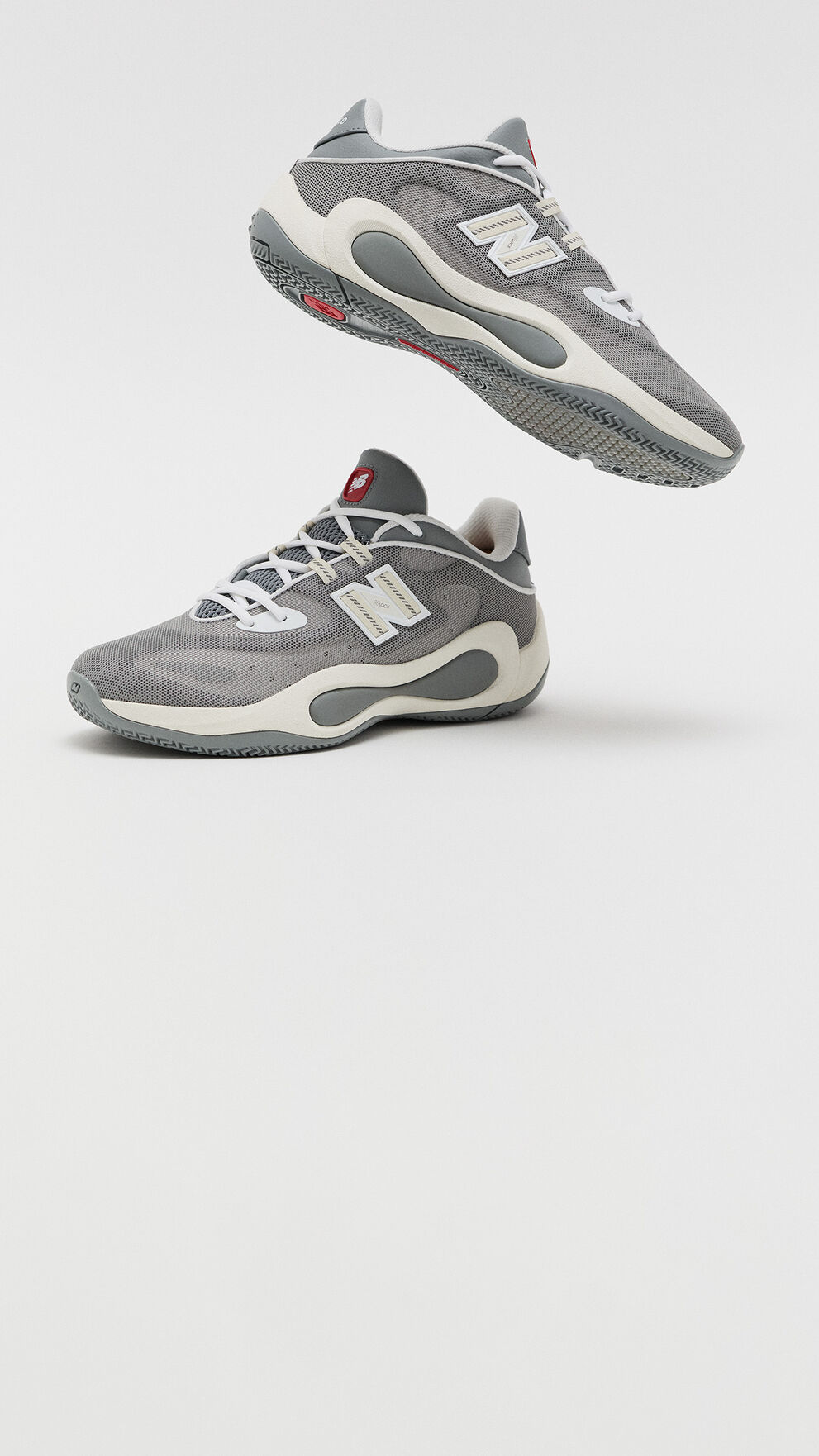 Gray New Balance athletic sneakers shown from side and underside angles, featuring a breathable mesh upper, white laces, and sculpted cushioned soles.